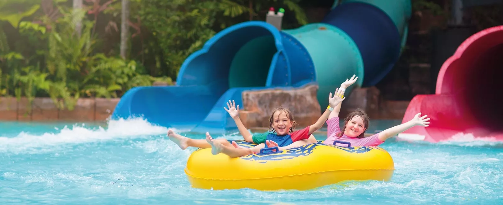 Deux enfants sur une bouée jaune dans une piscine avec des toboggans derrière
