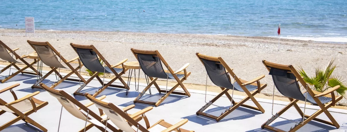 Une rangée de chaises en bois disposées sur le sable bordant la mer.