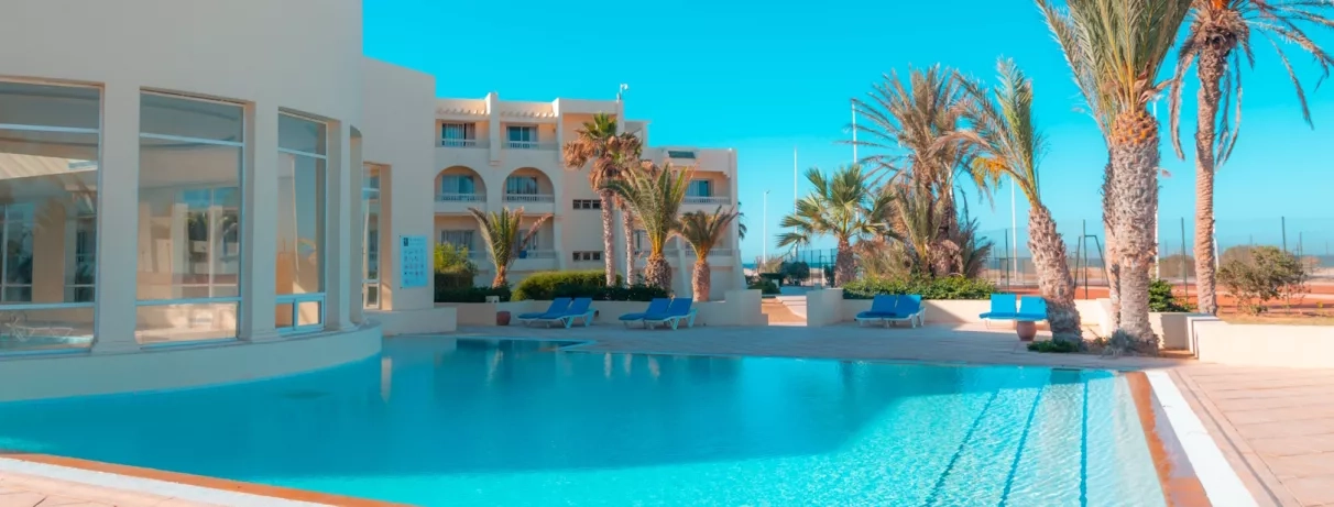 Bassin extérieur moderne et palmiers sous un ciel bleu azur au Vincci Dar Midoun à Djerba.