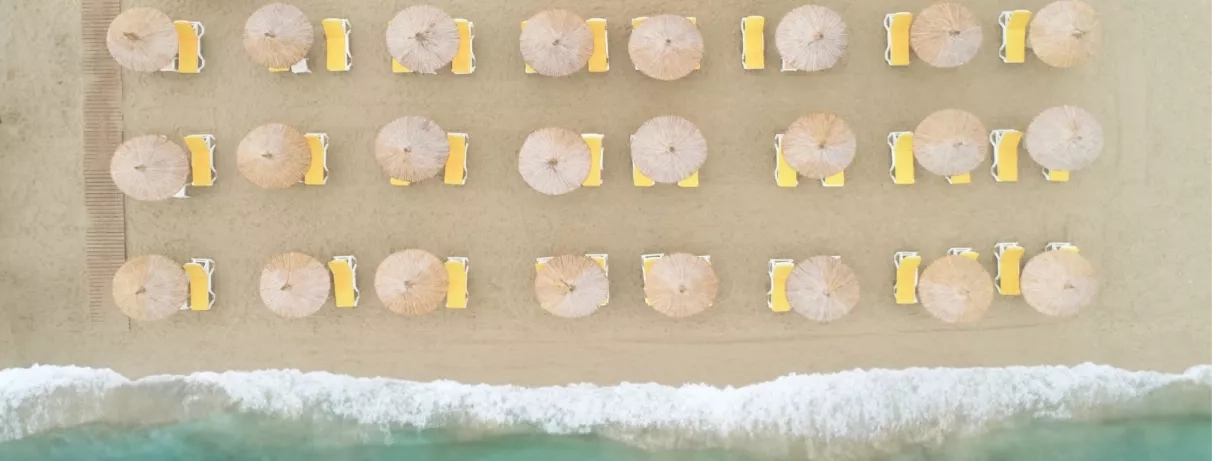Une vue de chaises longues et de parasols alignés sur une plage de sable fin en bord de mer.