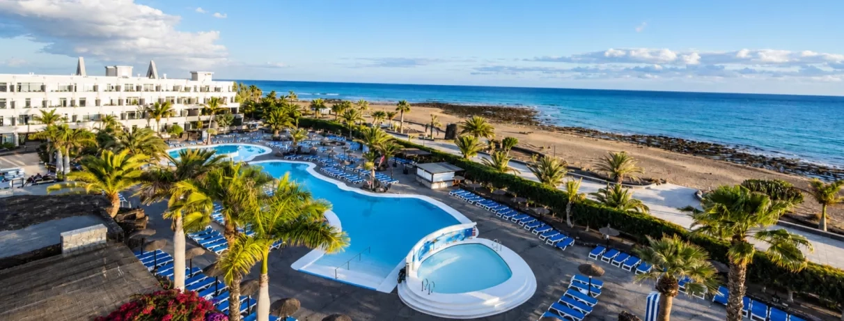Un panorama ensoleillé montrant une piscine, nichée entre des bâtiments d'hôtel et la mer.