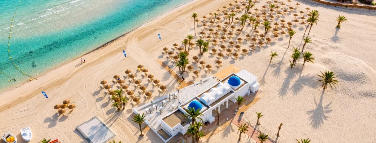 Plage aménagée avec transats et dômes bleus typiques face à la mer turquoise au Djerba Golf.