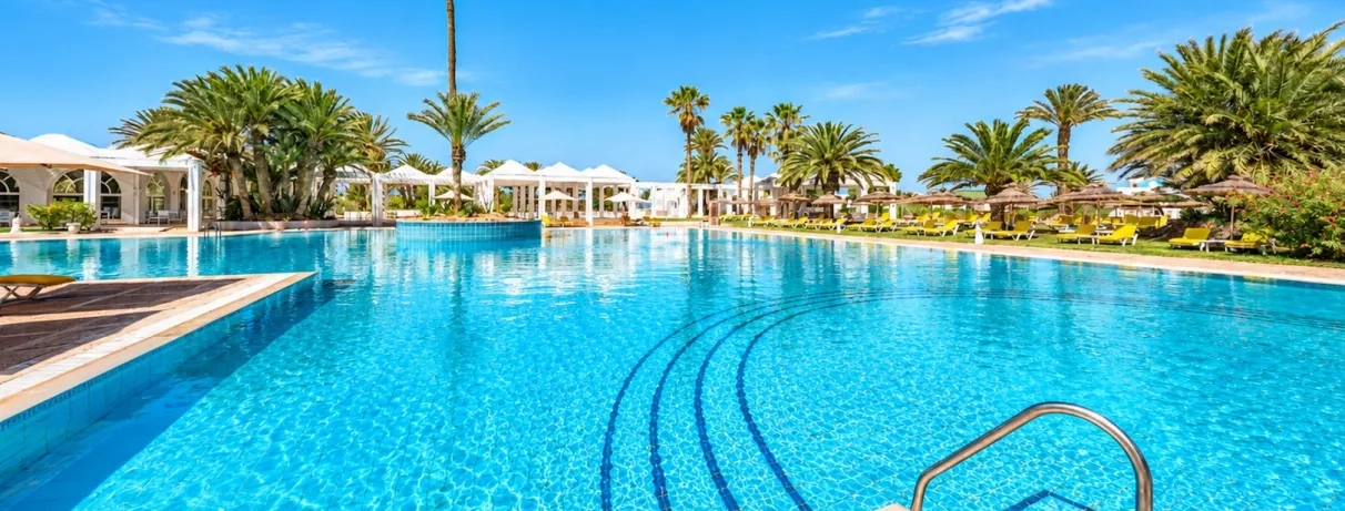Grande piscine extérieure entourée de palmiers et de transats sous le soleil au Djerba Golf.