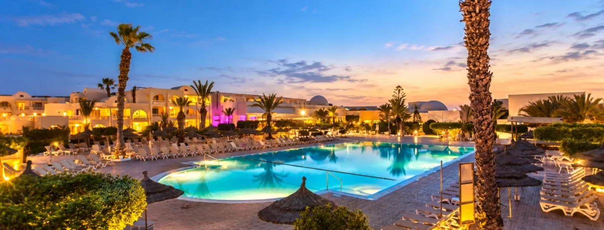 vue au coucher de soleil de la piscine avec palmiers et façade de l'hôtel du Djerba Aqua Resort à Djerba en Tunisie