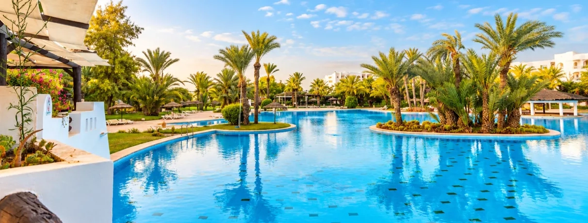 Vue panoramique sur la piscine lagon et les jardins tropicaux du Djerba Resort sous le soleil.