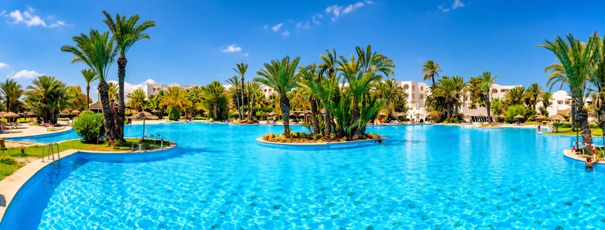 Vaste piscine turquoise entourée de palmiers et d'architecture traditionnelle à Djerba pour des vacances de détente.