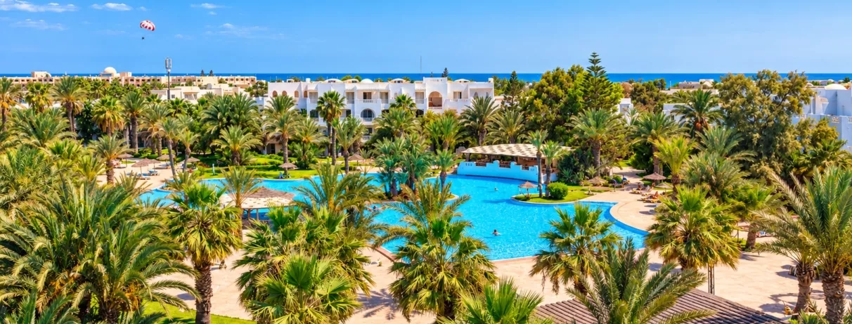 Grande piscine extérieure au coucher du soleil avec transats et parasols de paille au Djerba Resort.