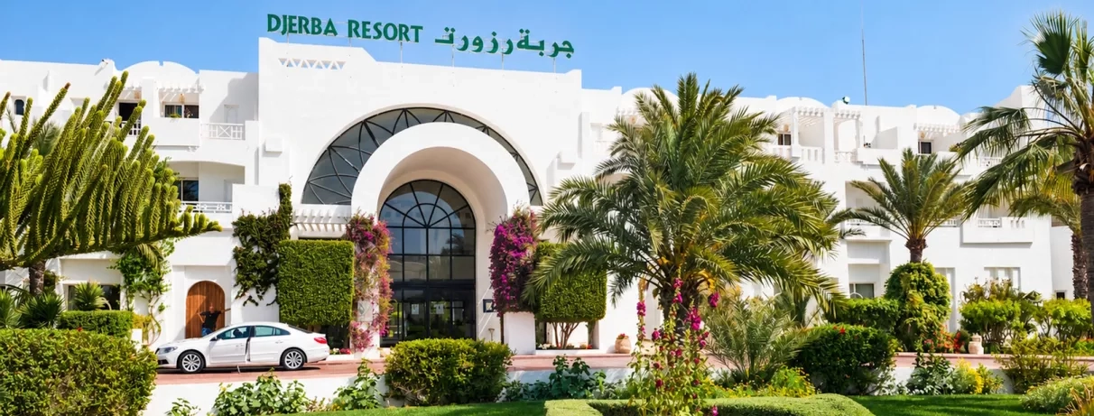 Façade blanche typique du Djerba Resort à Djerba, Tunisie, entourée de palmiers pour un séjour balnéaire.