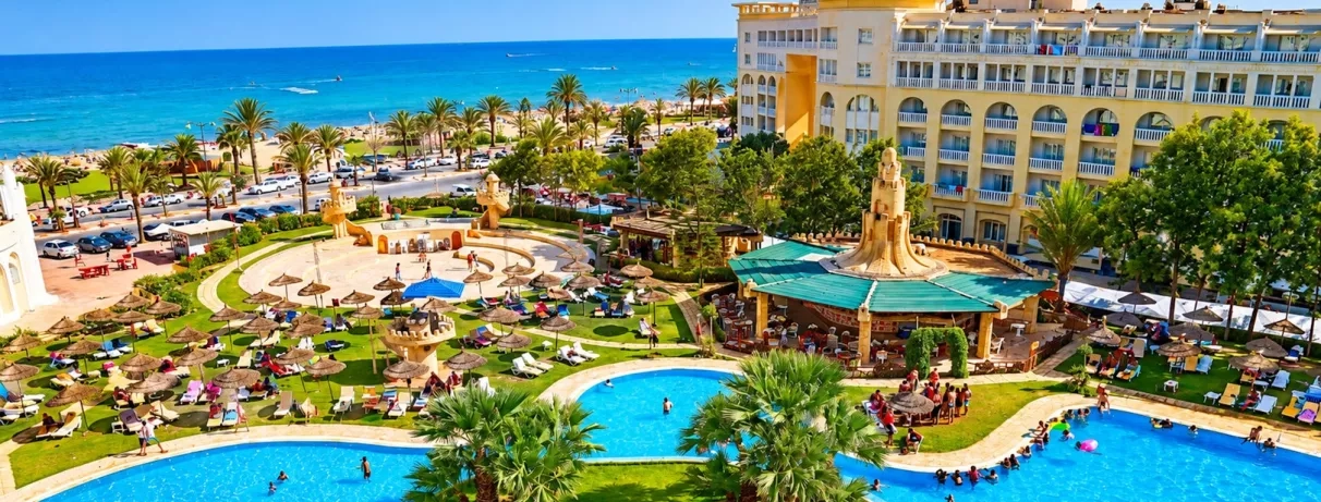 Vue générale de l’hôtel mettant en valeur la piscine extérieure, le bâtiment principal et la vue sur la plage.