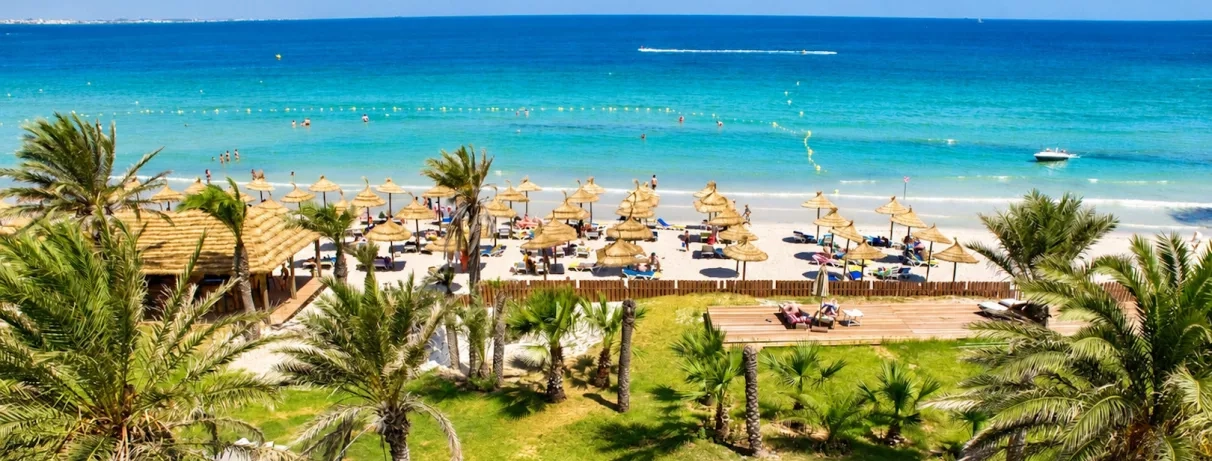 Plage de sable fin avec parasols en paille et mer turquoise au complexe hôtelier Royal Thalassa Monastir.