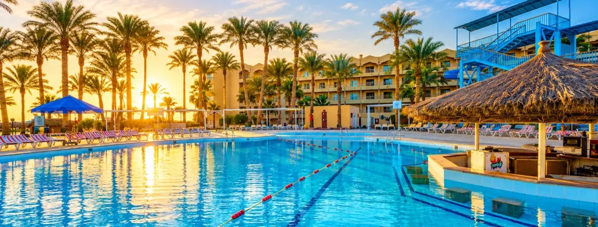 vue piscine extérieur avec bar central, transats autour, coucher de soleil, palmier, bâtiment de l'hôtel