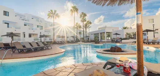 vue sur la piscine  avec transats et palmiers et coucher de soleil