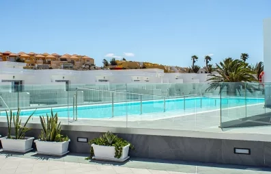 Une piscine aux eaux turquoise est entourée de rangées de plantes, sous un ciel bleu.