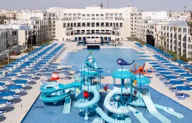 vue panoramique terrasse extérieure piscines tobogans bleus paraols et transats bleu blanc batiments blancs façade hôtel