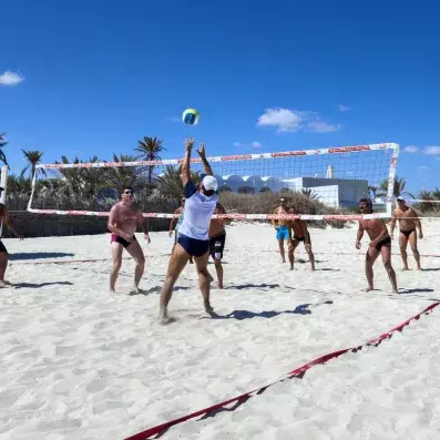 Match de beach‑volley sur plage ensoleillée avec joueurs en action et palmiers.