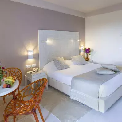 Chambre d’hôtel élégante avec lit double, lampes murales et coin détente avec fleurs et fruits.