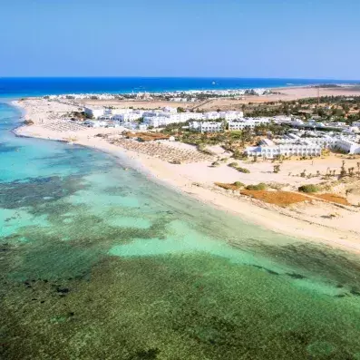 ue aérienne d’un resort en bord de mer avec plage de sable, eau turquoise et bâtiments blancs.
