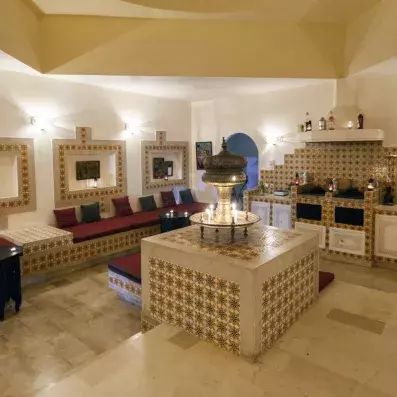 Salon de style oriental avec banquettes, lanternes en métal, carreaux décoratifs et niches éclairées.