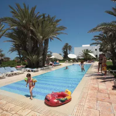 Piscine extérieure familiale avec palmiers, transats, parasols et enfant sortant de l’eau