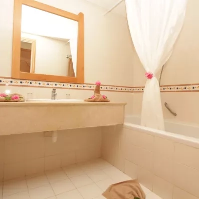 Salle de bain de l'hôtel avec baignoire, grand miroir encadré de bois et décoration soignée avec des fleurs fraîches et des serviettes pliées pour un accueil de bienvenue.