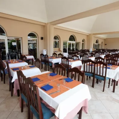 Salle de restaurant intérieure de l'hôtel avec de grandes tables dressées, chaises en bois sombre et arcades architecturales typiques.