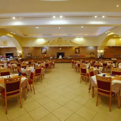 Vaste salle à manger principale de l'hôtel avec buffet central, éclairage chaleureux et décoration murale inspirée du patrimoine de Zarzis.