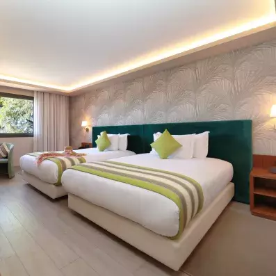 La chambre de l'hôtel avec deux lits de une place et demi séparés, avec des têtes de lits en vert foncé et du papier peint au mur. Une fenêtre donnant sur le jardin