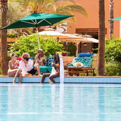 des gens au bord de la piscine sous un parasol vert profitant du solei
