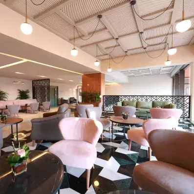 hall d'entrée décoré avec des chaises en rose, vert et gris et des tables basses et des plantes au milieu