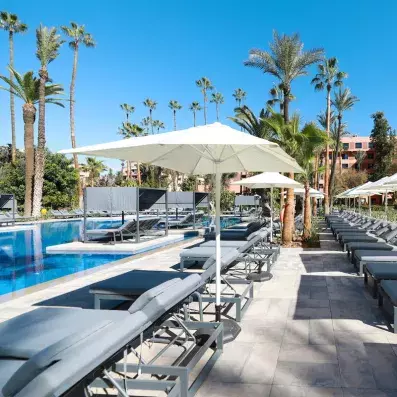 La piscine extérieur de l'hôtel et transats au bords avec des parasols et des palmiers