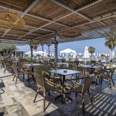 Un espace de restauration ombragé sous une structure en bois à proximité de la piscine.