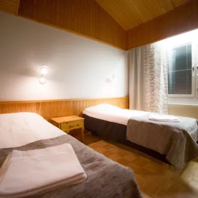 Chambre d'hôtel confortable avec lits jumeaux et boiseries offrant une ambiance cosy au Samperin Savotta, Finlande.