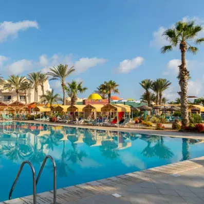 Grande piscine de resort entourée de cabanas jaunes, palmiers et transats, avec ciel bleu et ambiance tropicale relaxante.