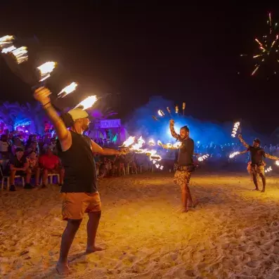 Spectacle nocturne de danse de feu sur la plage avec public et éclairages colorés.