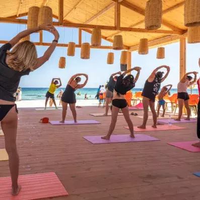 Cours de yoga en groupe sous pavillon en bois avec vue sur la plage.
