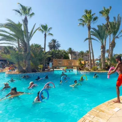 Séance d’aquagym dans piscine de resort avec participants et palmiers en arrière-plan.