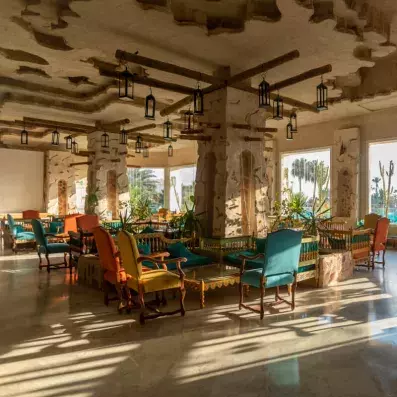 Espace lounge lumineux avec fauteuils colorés, tables en bois et grandes fenêtres donnant sur une végétation tropicale.