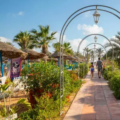 Allée pavée bordée de palmiers et lanternes décoratives menant à une plage tropicale.
