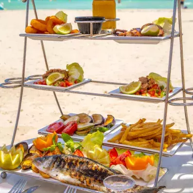Plateau de fruits de mer servi en étages face à la plage, avec poisson grillé, salades et calamars.