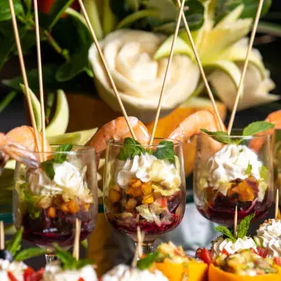Verrines gastronomiques décorées de crevettes, crème et fruits sculptés en arrière-plan.
