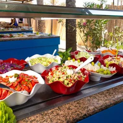 Buffet de salades fraîches en plein air avec légumes variés, fruits et plats colorés présentés dans des bols décoratifs dans une ambiance tropicale.