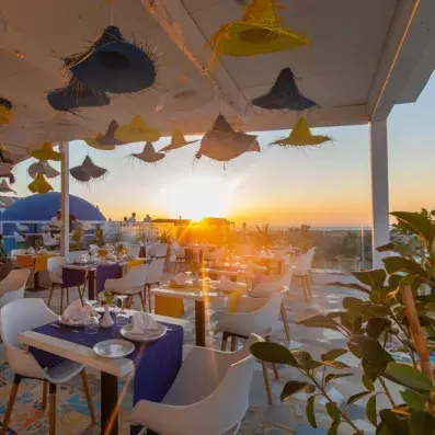 Espace de restauration extérieur au coucher du soleil avec tables dressées et vue sur l’océan.