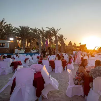 Dîner sur la plage avec tables décorées, invités et ambiance dorée au coucher du soleil.
