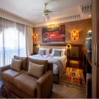 Chambre avec lit double, une fenêtre lumineuse à gauche et un canapé en beige devant le lit