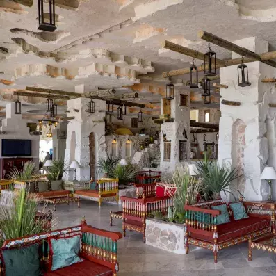 Salon traditionnel avec bancs en bois sculpté, lanternes suspendues et murs en pierre texturée.