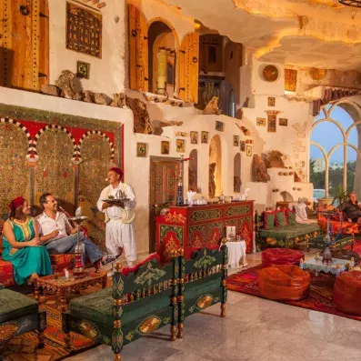 Restaurant traditionnel avec murs en pierre, tapisseries géométriques et tables élégamment dressées.