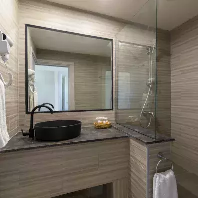Salle de bain moderne avec vasque noire, douche vitrée, murs effet bois et accessoires minimalistes.