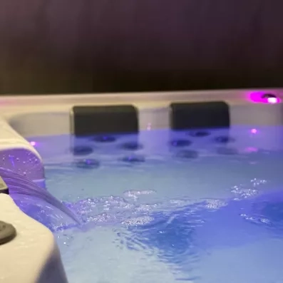 Jacuzzi intérieur avec jets d'eau et éclairage d'ambiance bleu et rose pour la relaxation.