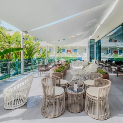 Une terrasse extérieure lumineuse et moderne, ombragée par de grandes voiles blanches.