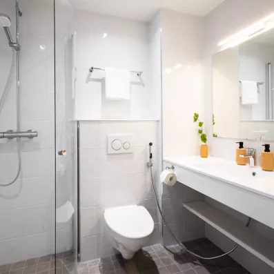 Salle de bain moderne et lumineuse de l'Hôtel Sodankylä avec douche à l'italienne, carrelage blanc et équipements contemporains.
